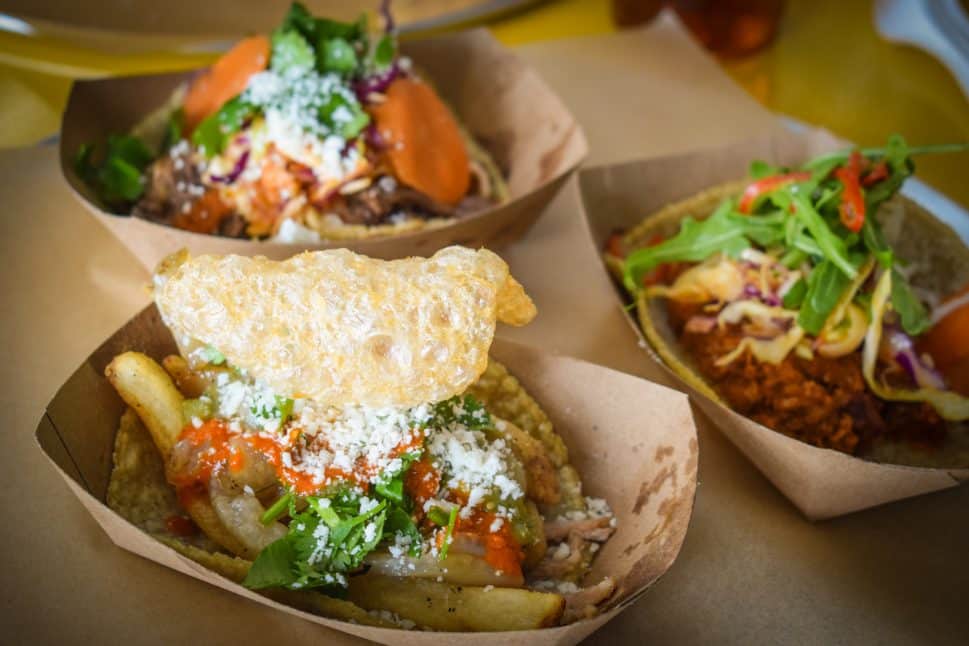 Three different tacos sit in individual paper trays.