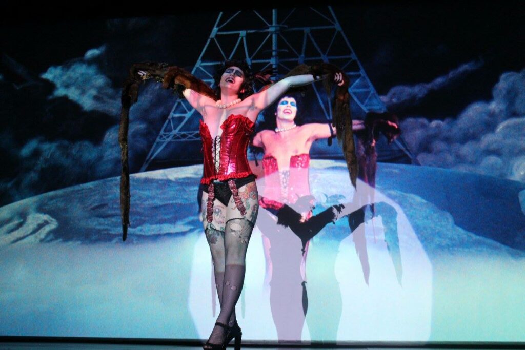 An actor is dressed in a red corset and fishnet tights as the character Frank N. Furtur from the Rocky Horror Picture Show.