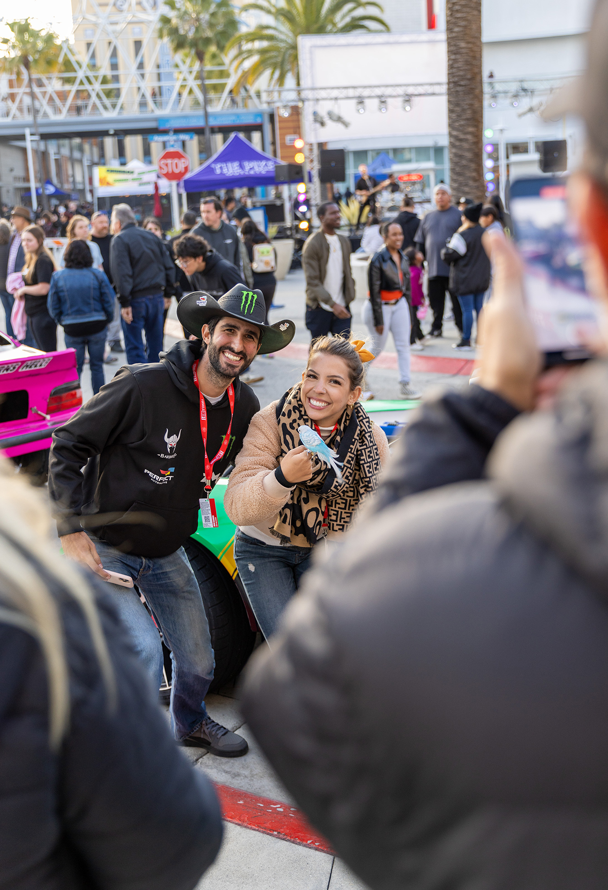 Joao Barion and Renata Ghiraldi pose with Beachy the parrot next to the race cars on display during Thunder Thursday at the Pike Outlets.