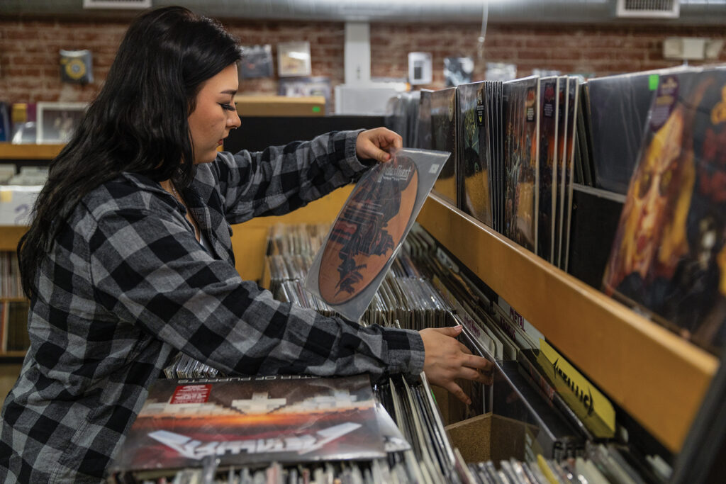 A young woman wearing a flannel shirt looks through vinyl records in a retail store.
