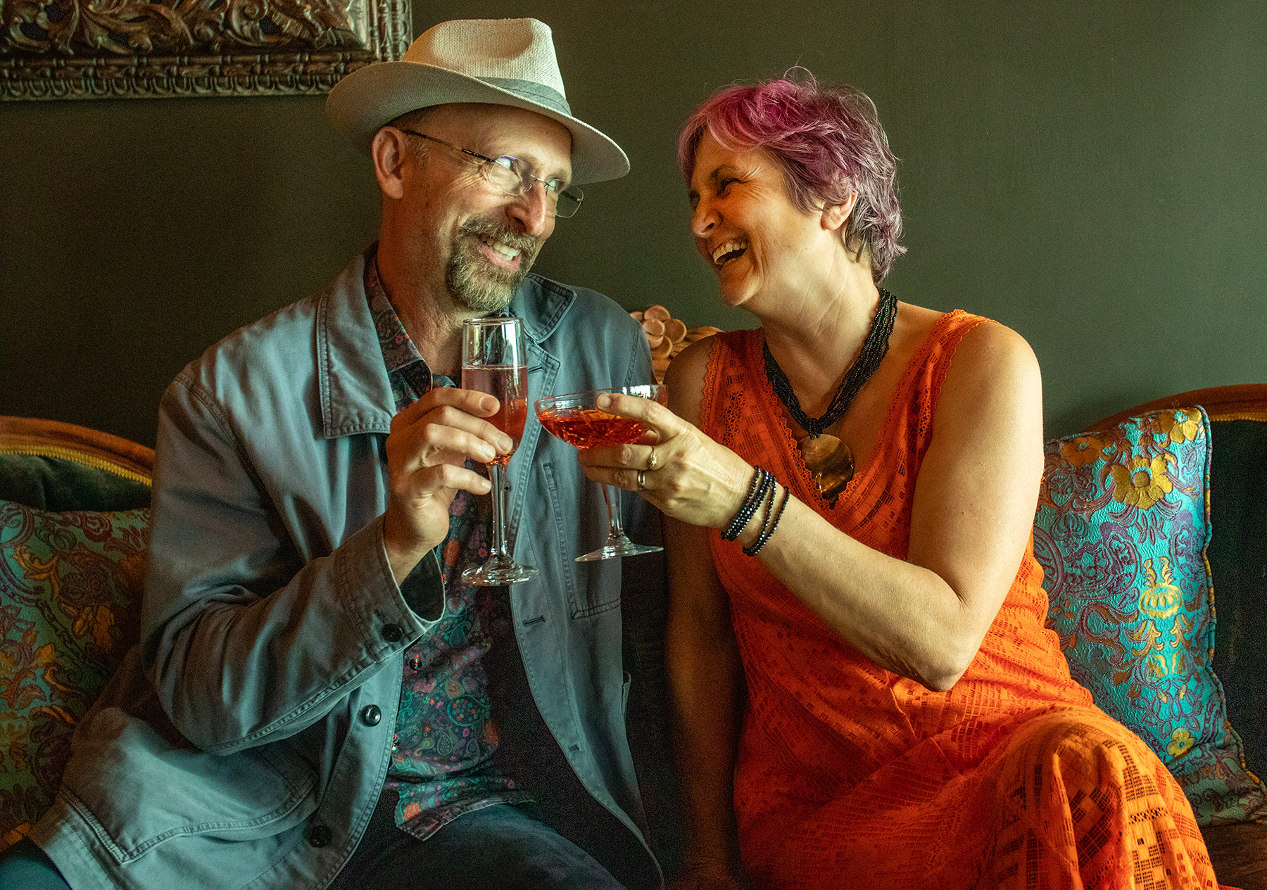 A man and a woman clink glasses and look at each other, smiling.