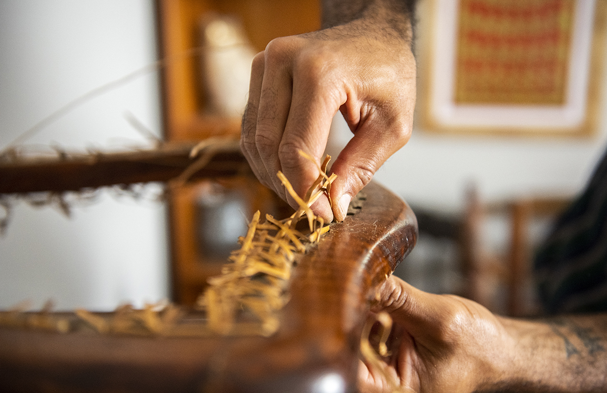 old brittle cane on a chair before threading new cane while working in his work studio.