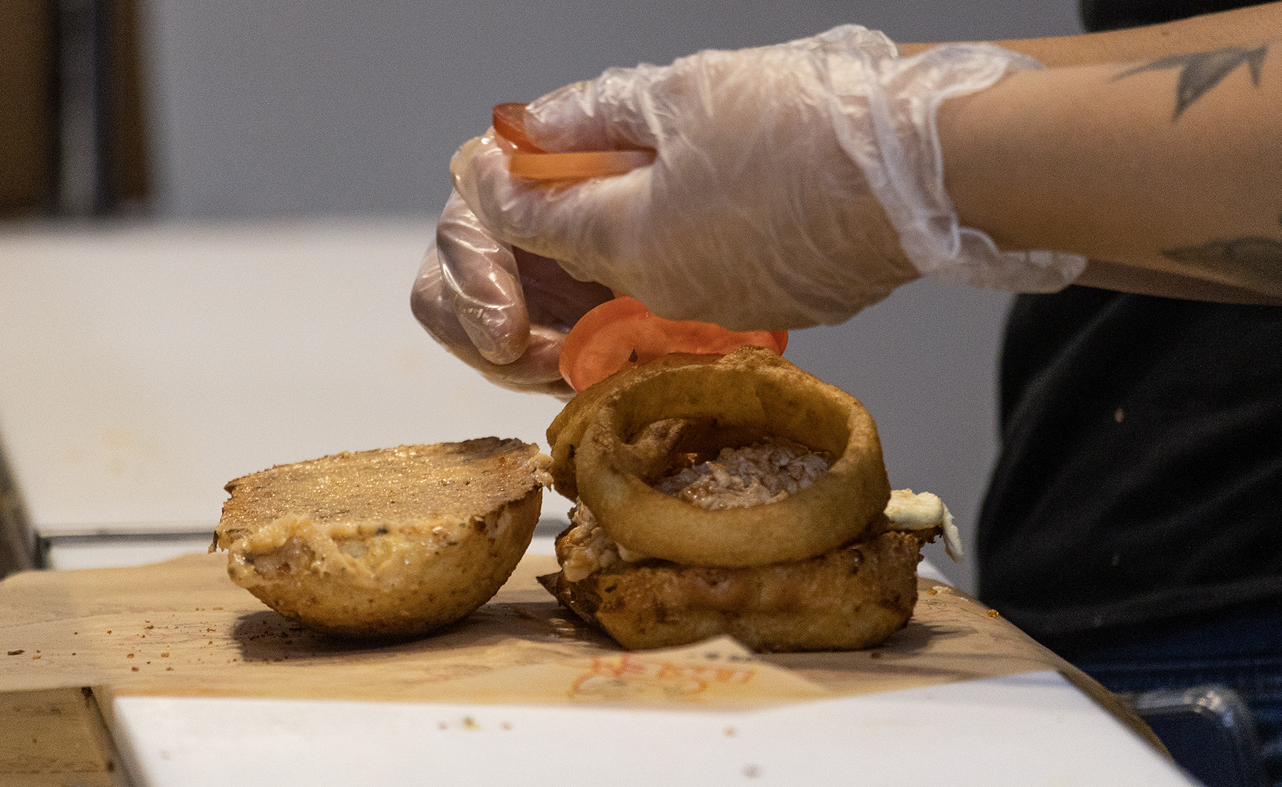 Two hands place tomatoes on a sandwich.