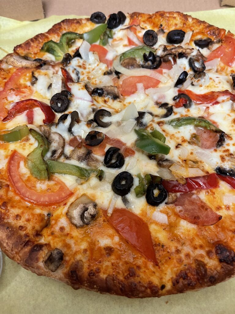 The pizza is topped with mozzarella cheese, green bell peppers, red bell peppers, onions, tomato, mushroom and olives.