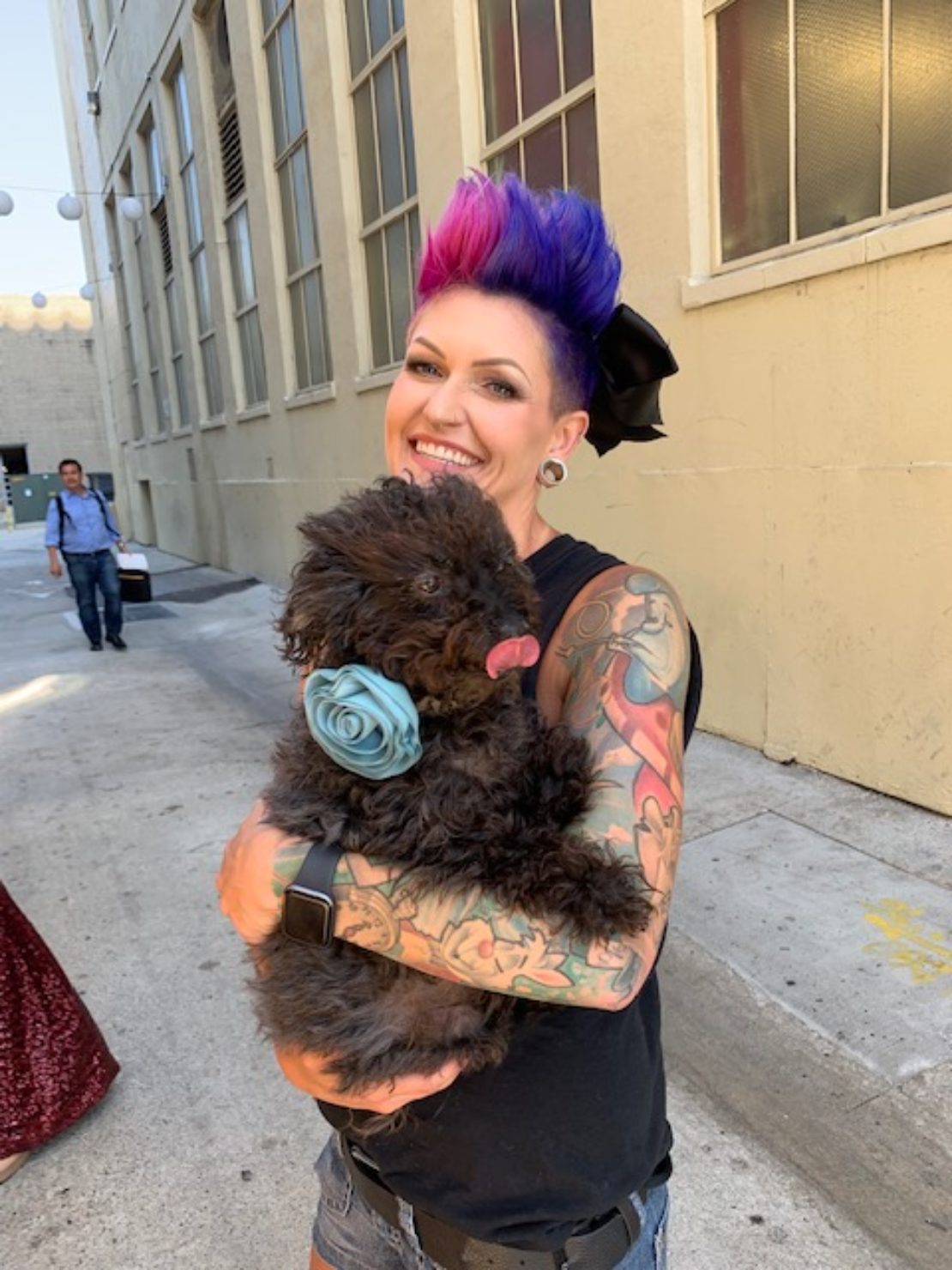 Woman with short magenta hair holds a little black poodle mix.