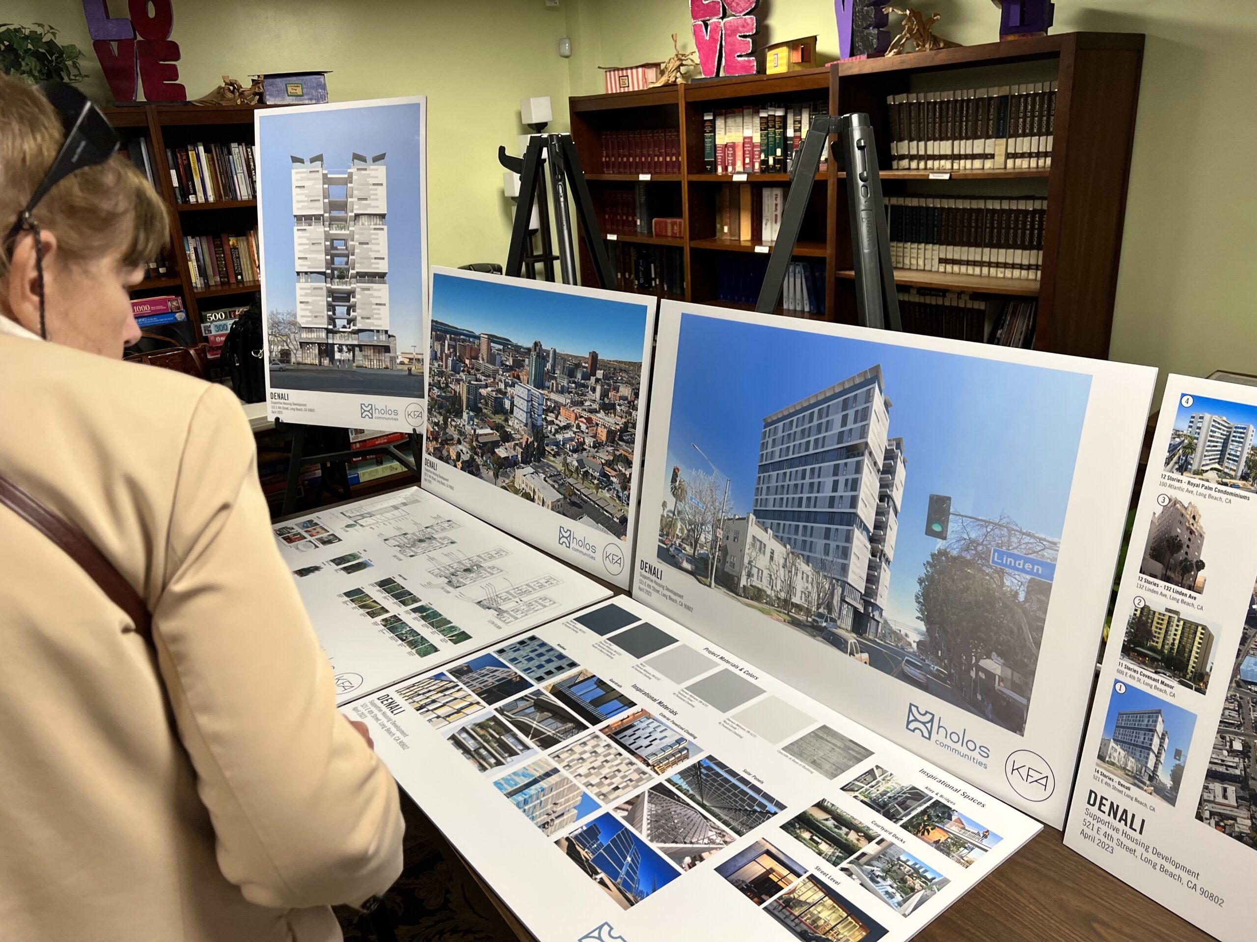 A woman in a light brown jacket looks at poster boards with the plans for the "Denali" housing project. 