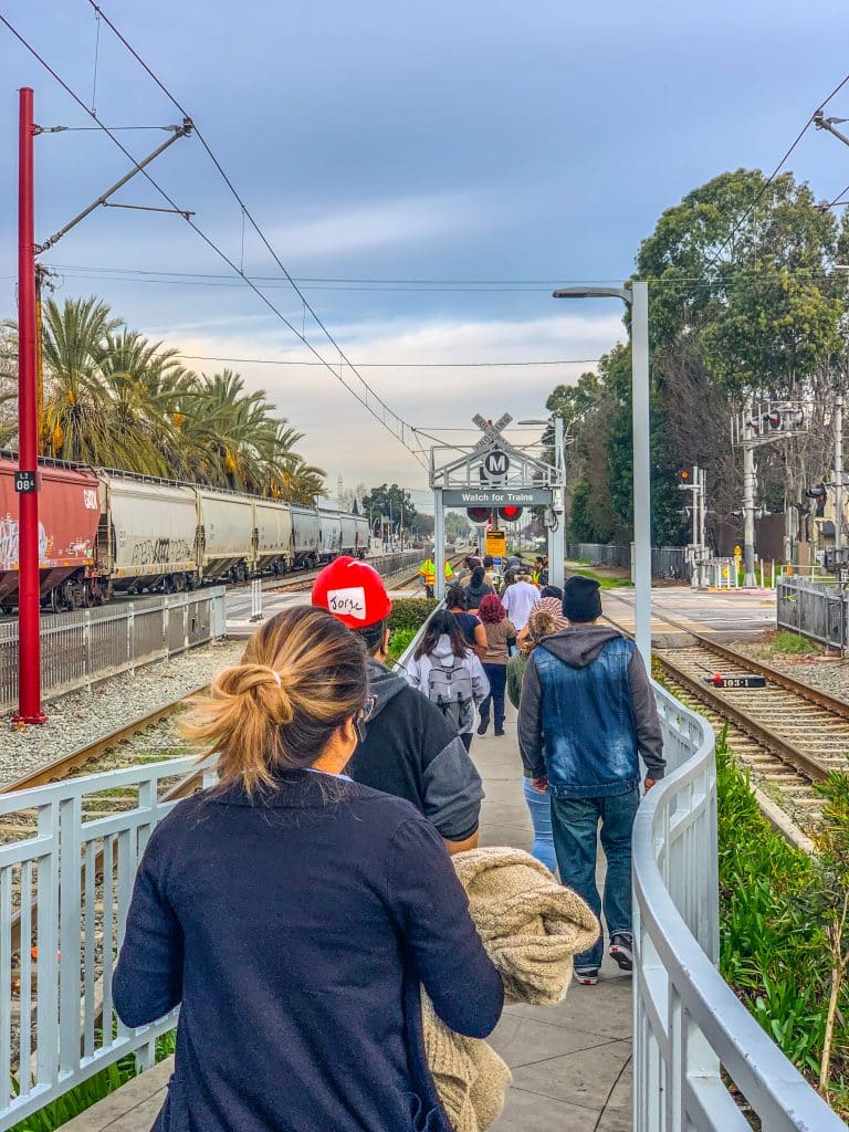 Blue Line riders, after exiting at the 103rd/Watts Towers station, wait to cross the tracks in order to access Metro's bus shuttles to continue their trip south. Photo by Brian Addison.
