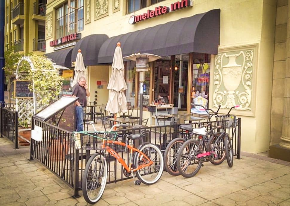 Patio space of restaurant is fenced with bikes locked to it and empty tables.