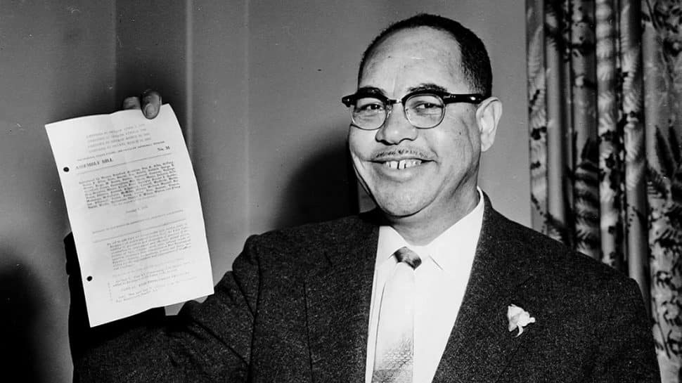 A black-and-white picture shows a black politician holding up a document.